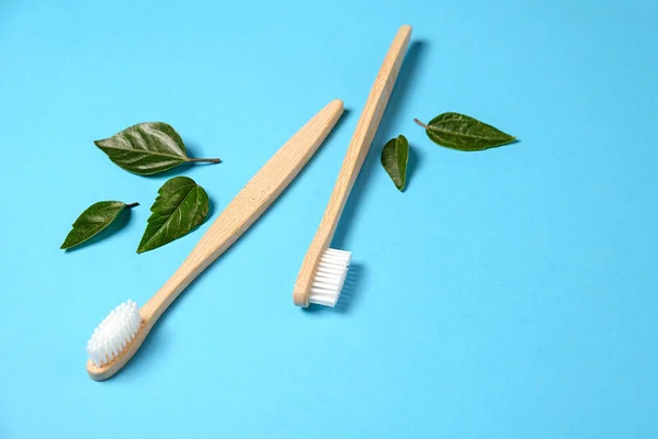 Dos cepillos de dientes ecológicos de bambú de madera y hoja verde sobre fondo azul. Cuidado dental y concepto de cero residuos. Plano, vista superior, espacio para copiar — Foto de Stock