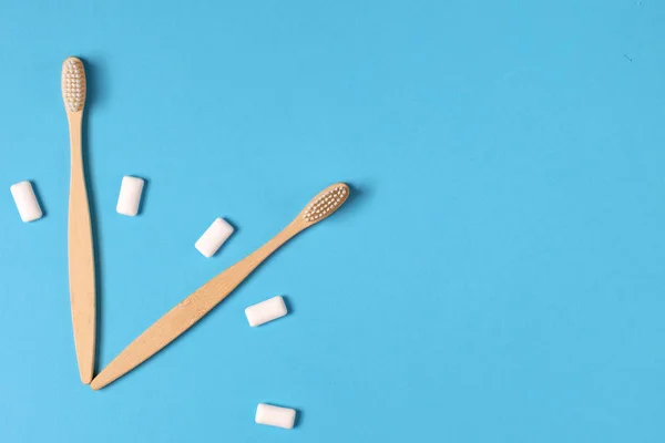 Two wooden bamboo eco friendly toothbrushes and chewing gum in the form of hours on a blue background. Eco friendly and reuse concept. Flat lay, top view, copy space — Stock Photo, Image