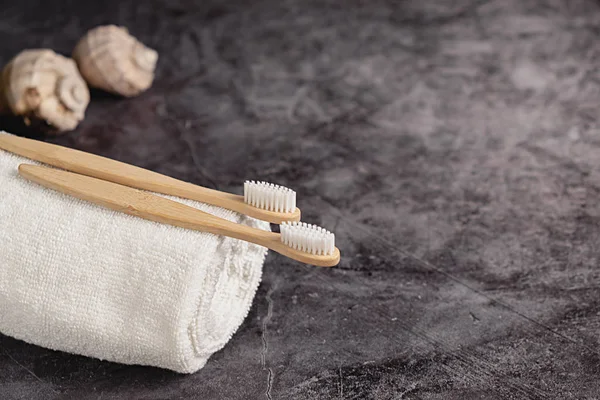 Två eco naturliga bambu tandborstar, snäcka, vit handduk på grå bakgrund. Hållbar livsstil och noll avfall hem. Tandvård och Miljövänlig och återanvändning koncept. Kopiera utrymme — Stockfoto