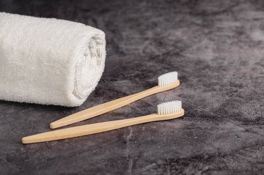 Gri arkaplanda iki doğal bambu diş fırçası ve beyaz havlu. Sürdürülebilir yaşam tarzı ve sıfır atık ev. Diş bakımı, çevre dostu ve yeniden kullanım konsepti. Boşluğu kopyala