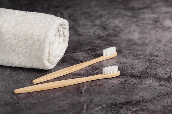 Två eco naturliga bambu tandborstar och vit handduk på grå bakgrund. Hållbar livsstil och noll avfall hem. Tandvård och Miljövänlig och återanvändning koncept. Kopiera utrymme — Stockfoto