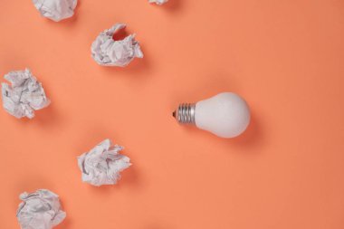 Buruşmuş ofis kağıdı ve turuncu arka planda beyaz ampul olan yeni bir fikir. Beyin fırtınası sırasında yaratıcı bir çözüm. Düz konum, üst görünüm, kopyalama alanı