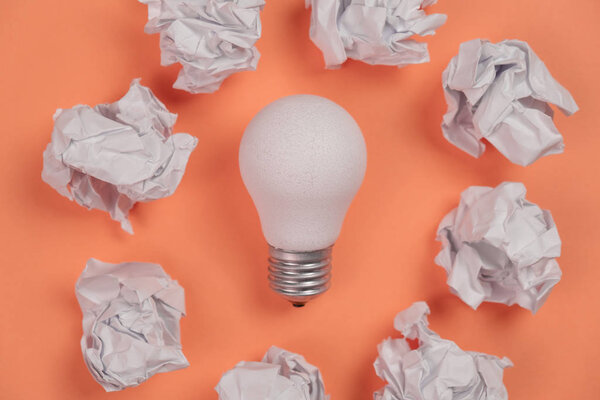 new idea concept with crumpled office paper and white light bulb on orange background. Creative solution during brainstorming session concept. Flat lay, top view, copy space