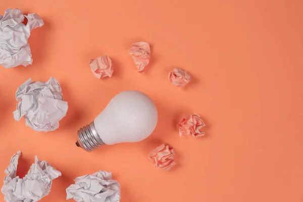 Neues Ideenkonzept mit zerknittertem Büropapier und weißer Glühbirne auf orangefarbenem Hintergrund. kreative Lösung während des Brainstormingkonzepts. flache Lage, Draufsicht, Kopierraum — Stockfoto