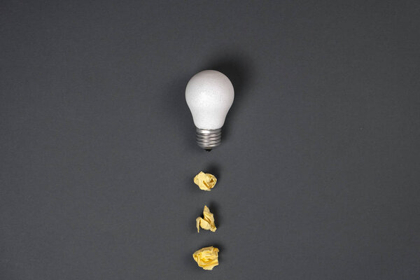 Creativity inspiration, great business idea concept with white light bulb and paper crumpled ball on gray background. Flat lay, top view, copy space