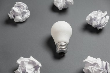 Buruşuk ofis kağıdı ve gri arka planda beyaz ampul olan yeni bir fikir. Beyin fırtınası sırasında yaratıcı bir çözüm. Düz konum, üst görünüm, kopyalama alanı