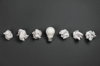 Buruşuk ofis kağıdı ve gri arka planda beyaz ampul olan yeni bir fikir. Beyin fırtınası sırasında yaratıcı bir çözüm. Düz konum, üst görünüm, kopyalama alanı