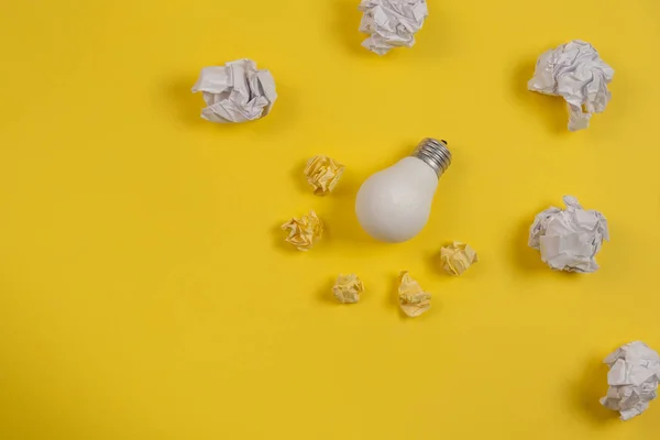 Neues Ideenkonzept mit zerknittertem Büropapier und weißer Glühbirne auf gelbem Hintergrund. kreative Lösung während des Brainstormingkonzepts. flache Lage, Draufsicht, Kopierraum — Stockfoto