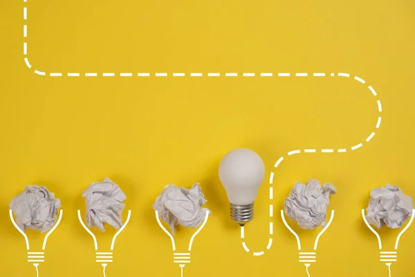 新概念与皱折的办公室纸和黄色背景的白色灯泡。 脑力激荡过程中的创造性解决方案. 平面布局，顶视图，复制空间 — 图库照片