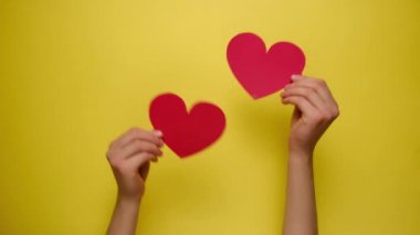Sarı kağıt duvarın içinden kırmızı kağıt kalpler tutan kadınların ellerini kapatın. Sevgililer Günü ve Anneler Günü veya Hayat Mutluluğu Konsepti.