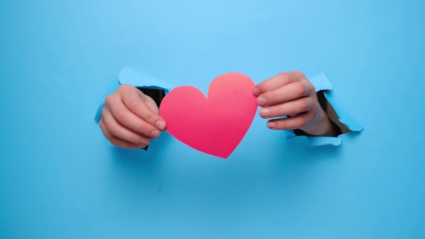 度假背景 通过撕破的蓝色纸墙 将手牵着红纸心的女性的手合拢在一起 情人节和喜欢写博客的社交网络温情的概念 — 图库视频影像