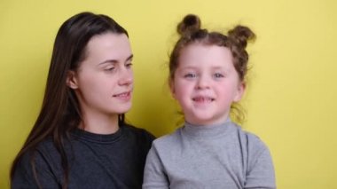 Neşeli pozitif anne ve kız kameraya bakıyor, çocuklu anneye gülümsüyor, video görüşmesi yapıyor, aile video blogcuları video blogu ya da video blogu kaydediyor, arka planda sarı duvarda oturuyor.