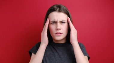 Hayal kırıklığına uğramış bir kadın alnının üstünde el ele tutuşuyor, baş ağrısı çektiği için depresyona giriyor, gri tişört giyiyor, kırmızı arka planda duruyor. Negatif insani duygular ve duygular