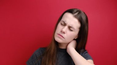 Yorgun genç bir kadın boynu ağrıyan sert bir kavram hissediyor masaj yapan gergin kaslar fibromiyaljiden muzdarip, kasvetli bir ifadesi var, kırmızı arka planda izole edilmiş. Fibromiyalji kavramı