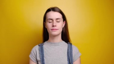 Tişörtlü ve kot pantolonlu çekici bir kadın yoga yapıyor. Egzersiz yapıyor. Sarı arka plan üzerinde meditasyon yapıyor.