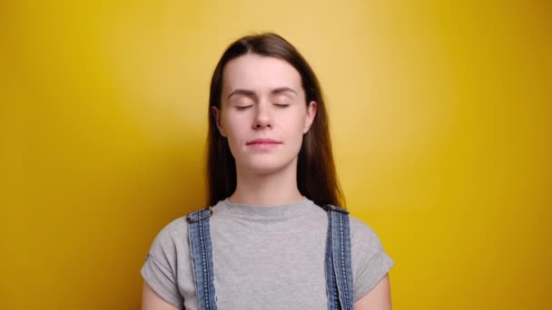 Tシャツとデニム全体で魅力的な女性ヨガの練習の女の子瞑想黄色の背景の上に立って閉じ目は内部バランスを感じます指泥ジェスチャー いいえストレスコンセプト — ストック動画