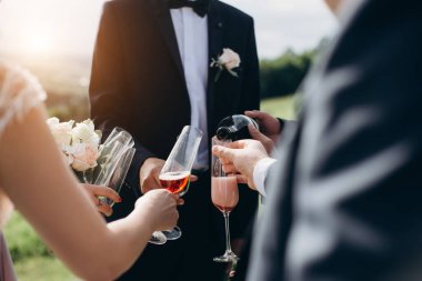 Gün batımında kırmızı şampanyalı bardakları olan bir grup insanın görüntüsü. Arkadaşlar önemli bir olayı kutluyor.