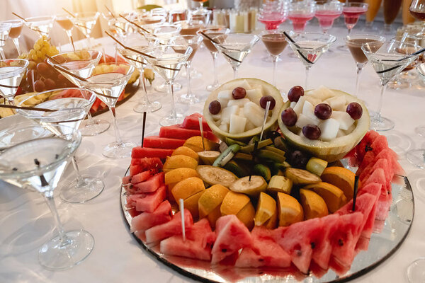 Festive table with cold exotic alcoholic beverages, cocktails, watermelon, grape, banana and different fresh fruits. Celebration or other event