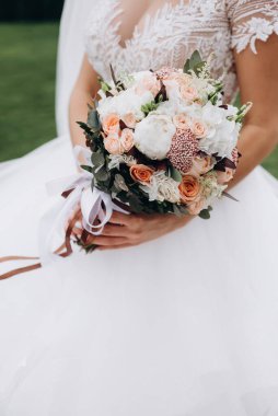 Düğün detayları. Gelin ellerini kapayarak modern, şık bir buket beyaz, sarı güller ve okaliptüs yeşiliyle kaplayın. Yaz çiçekli kompozisyon.