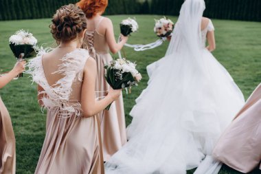 Zarif nedimelerin arka manzarası açık havada yeşil çimlerde yürümeleri ve güzel modern bir düğün buketi tutmaları..