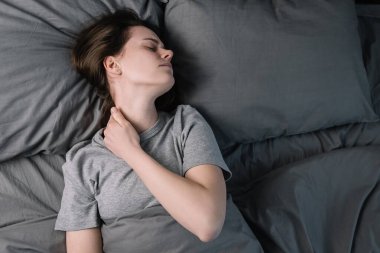 Üzgün, gözleri kapalı bir kadın. Boyun kasları gergin. Yatakta yatıyor. Stres atağı, acı çeken bitkin bir kız. Fibromiyalji kavramı