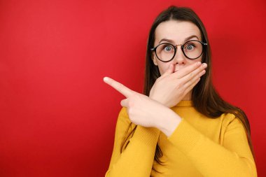 Gözlüklü genç bayanın hayret verici bir ifadesi var. Reklamınız ya da tanıtımınız için boş bir fotokopi alanı gösteriyor. Sarı kazak giyiyor, kırmızı stüdyo arka planında poz veriyor.