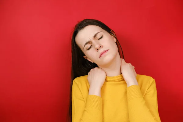 心烦意乱的年轻女子感到僵硬的脖子疼痛概念按摩紧张肌肉患有纤维肌痛 有忧郁的表情 孤立在红底 纤维肌痛的概念 — 图库照片