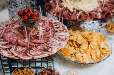 Peynirli ziyafet masasını kapatın, kalçalar, fındıklar, soğuk etler, dilimlenmiş sosisler, salatalıklar, domatesler. Lezzetli çerezlerin çeşitleri. Yiyecek konsepti