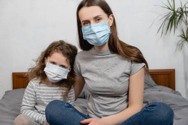 Ön tarafı kapatın. Anne ve küçük kız yüz maskesi takıyor. Kameraya bakın. COVID-19 sars-cov-2 salgın virüs salgını koruma kavramı