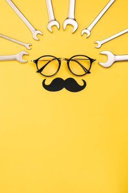 Şeffaf gözlüklü yaratıcı düz konum, şık siyah fotoğraf kabini bıyıkları ve sarı arkaplan fotokopi alanındaki kombinasyon anahtarlarını destekliyor. Babalar Günü erkeklik konsepti blogu