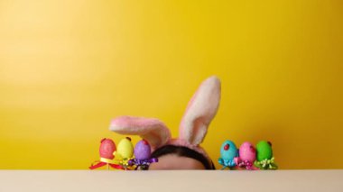 Çekici, neşeli, genç bir kadın Paskalya yumurtası avlamaya başlar, tüylü kulaklar takar, sarı arka planda fotokopi çekerek poz verir. Mevsimlik tatil konsepti. Mutlu Paskalyalar!