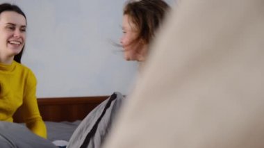 Mutlu anne ve aktif çocuk yatakta komik yastık oynuyorlar. Genç anne ve küçük kız çocuk yatak odasında birlikte eğleniyorlar. Seçici odaklanma. Kişisel tecrit, ev karantinası.