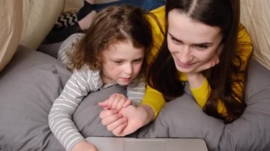 Sevgi dolu genç bir anne ve küçük tatlı bir kızın çocuk odasında çadırda oturup dizüstü bilgisayarla eğlenmesi çevrimiçi eğitim programı izlemesi. Aile birlikte vakit geçirmekten hoşlanır.
