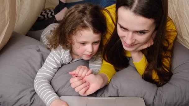 用笔记本电脑观看卡通片在线教育节目 在儿童房的帐篷里 亲热的年轻妈妈和可爱的小女儿坐在一起玩乐的场景 家人在一起很开心 — 图库视频影像
