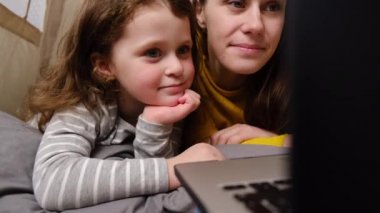 Çocuk odasında çadırda oturmuş dizüstü bilgisayarla internetten eğitim programı izleyerek eğlenen sevimli küçük bir kızı olan genç anneyi çok seviyorum. Aile birlikte vakit geçirmekten hoşlanır.