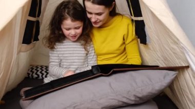 Sevgi dolu bir anne ve sevimli küçük bir kız çocuğu çadırda oturuyor, fotoğraf albümü seyrediyor, genç bir aile birlikte eğleniyor. Kişisel tecrit, ev karantinası.