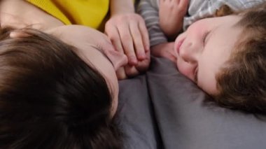 Gülümseyen tatlı kızı olan mutlu genç bir anne rahat bir yatakta dinleniyor, anne ya da dadı dinleniyor ve küçük kızıyla konuşuyor, yatak odasında sakin bir hafta sonu geçiriyor. seçici odak
