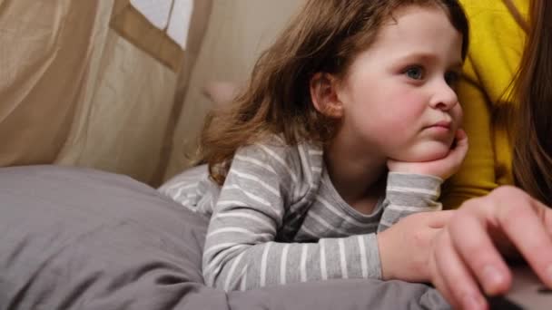 Souriant jeune mère et petite fille enfant s'amuser à regarder un ordinateur portable, assis dans une tente, maman heureuse enseignant enfant fille utiliser application ordinateur portable, regarder un dessin animé ou faire un appel vidéo sur ordinateur 
