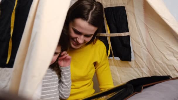 幸せな愛情のある若い母親とかわいい娘が一緒にホームビューの写真アルバムにテントに座っているのを閉じると お母さんは就学前の子供と楽しい時間を過ごしています 隔離室隔離室 — ストック動画