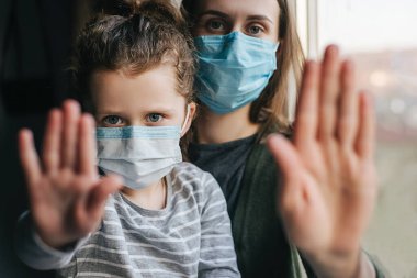 Evdeki pencerenin pervazında oturan üzgün küçük kız ve anne portresini kapatın. Korunmak için maske takın ve Coronavirus salgınını durdurmak için el hareketlerini durdurun. Kişisel tecrit, ev karantinası.