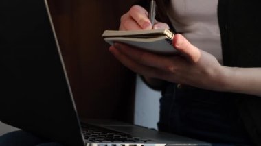 Dizüstü bilgisayarını kapat, önemli verileri not defterine yaz, modern bilgisayarda çalışan ya da online not bilgisi okuyan, pencere pervazında oturan bir kadın. Sosyal uzaklık kavramı