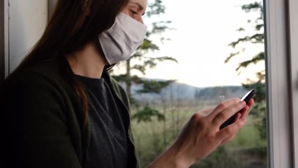 Jonge Vrouw Met Gezichtsmasker Vensterbank Thuis Kijkend Naar Telefoon Chatten — Stockvideo