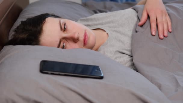 躺在床上看着智能手机的疲惫而沮丧的年轻女性的侧面视角会感到害怕和害怕 不快乐的焦虑会导致人际关系出现问题 受害者会害怕打电话或发短信 — 图库视频影像