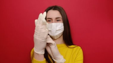 Ciddi genç kadınlar koruyucu beyaz bir maske takarak diğer insanlara bulaşmaz, tıbbi eldiven takar, koronavirüs salgınına hazırlanır, kırmızı arka planda izole edilir. Karantina konsepti
