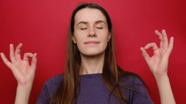 Mor tişörtlü güzel ve çekici bir kadın yoga yapıyor. Egzersiz yapıyor. Kırmızı arka planda meditasyon yapıyor.