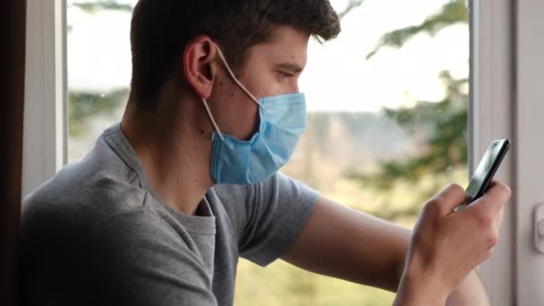 Anak Muda Mengenakan Masker Wajah Duduk Ambang Jendela Rumah Melihat — Stok Video