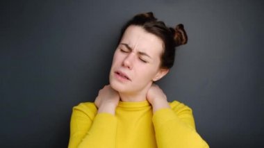 Üzgün genç bir kadın, boynu ağrıyan, masaj yapan, gergin kasları ovuşturan, fibromiyaljiden muzdarip, kasvetli bir ifadeye sahip, gri arka planda izole edilmiş. Fibromiyalji kavramı