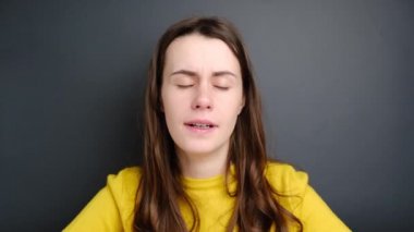 Uykulu bir kadın esniyor, sarı süveter giyiyor, gri arka planda izole edilmiş, uykulu, ilgisiz, uyuşuk, tembel, uykusuzluktan ağzı açık kalmış, uykusuzluktan acı çekiyor. Yorgunluk ve uyanış kavramı