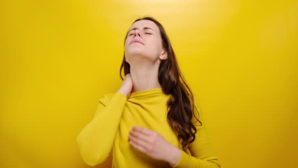 不健康な若い女性の緊張した首の筋肉をマッサージ 疲労した女の子の痛みに苦しんで 物理的な不快感を感じ 黄色のスタジオの背景に隔離された悲観的な表現をしています 線維筋痛症の概念 — ストック動画