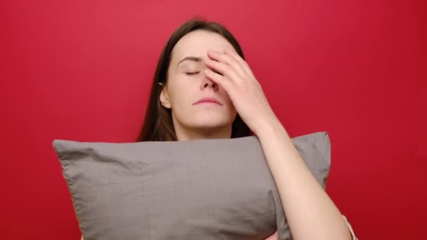 女性はあまりにも早起きのために 睡眠不足のために苦しんで強調した 不満若い女性は暗い顔をしており 灰色の枕を運ぶ 不眠症を持っており 夜遅く 赤の背景に隔離された眠りにつくことはできません — ストック動画